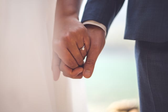 A couple holding hands with a ring on the woman's finger.