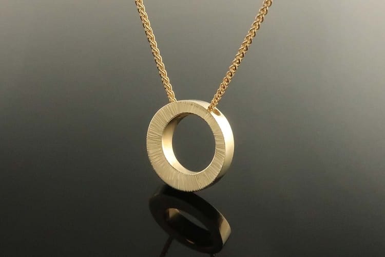 A simple gold necklace with a small, circular pendant made from a natural stone.