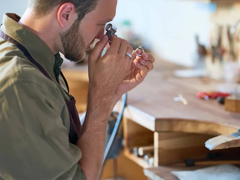 a person examining a piece of jewelry with a magnifying glass.