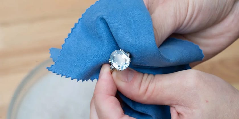 A close-up of a person's hands carefully storing jewelry in a soft cloth pouch.