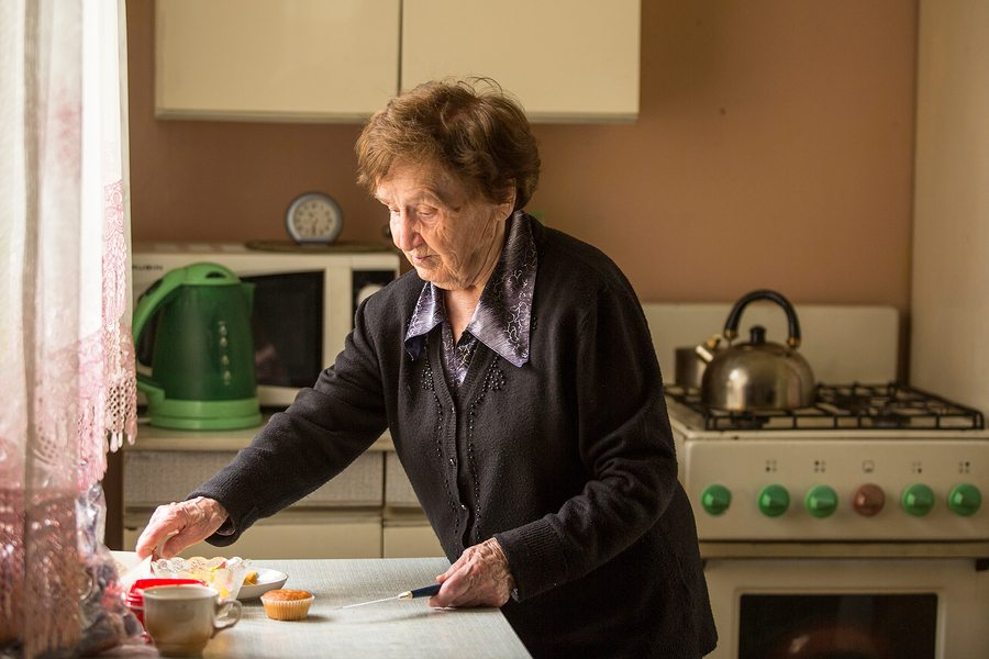 An elderly woman safely using a stove in her kitchen.